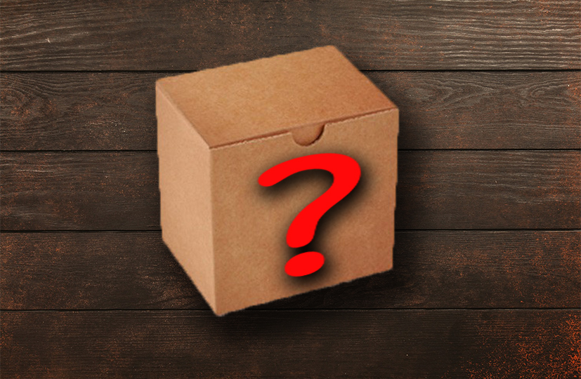 Una caja de cartón sin ningún tipo de identificación, con un signo de interrogación rojo en su frontal. De fondo, la superficie de una mesa de madera, de color marrón oscuro.